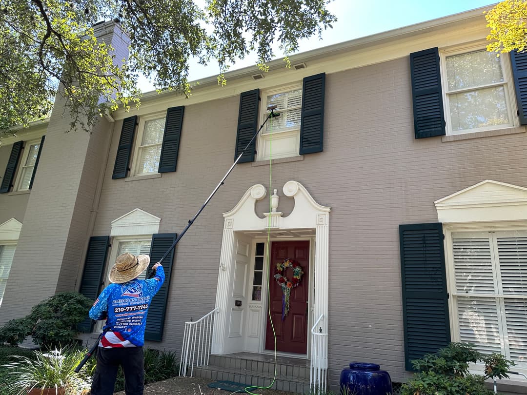 Person cleaning windows on a two-story house using a long pole with a brush.