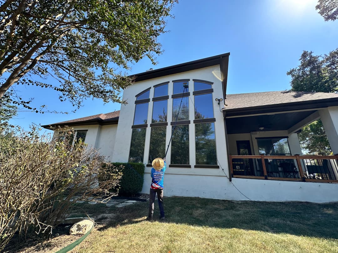 Child cleaning large windows of a modern house under a clear blue sky.